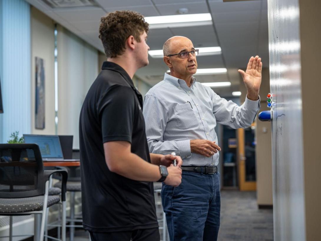 A School of Management Kettering professor explains a business concept to a student in front of a whiteboard