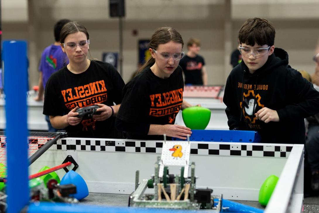 Three high school students wearing safety glasses watch their robot compete at the VEX State Championship at Kettering