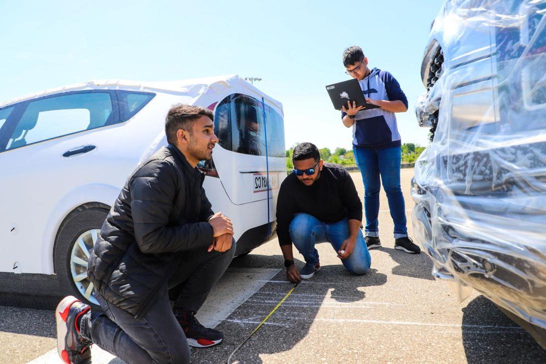 Three Kettering students at the Mobility Research Center measure markings on a road using measuring tape. One holds a laptop